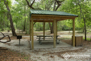 Royal Springs Picnic pavilion with table, grill, trash receptacle under big oak trees.